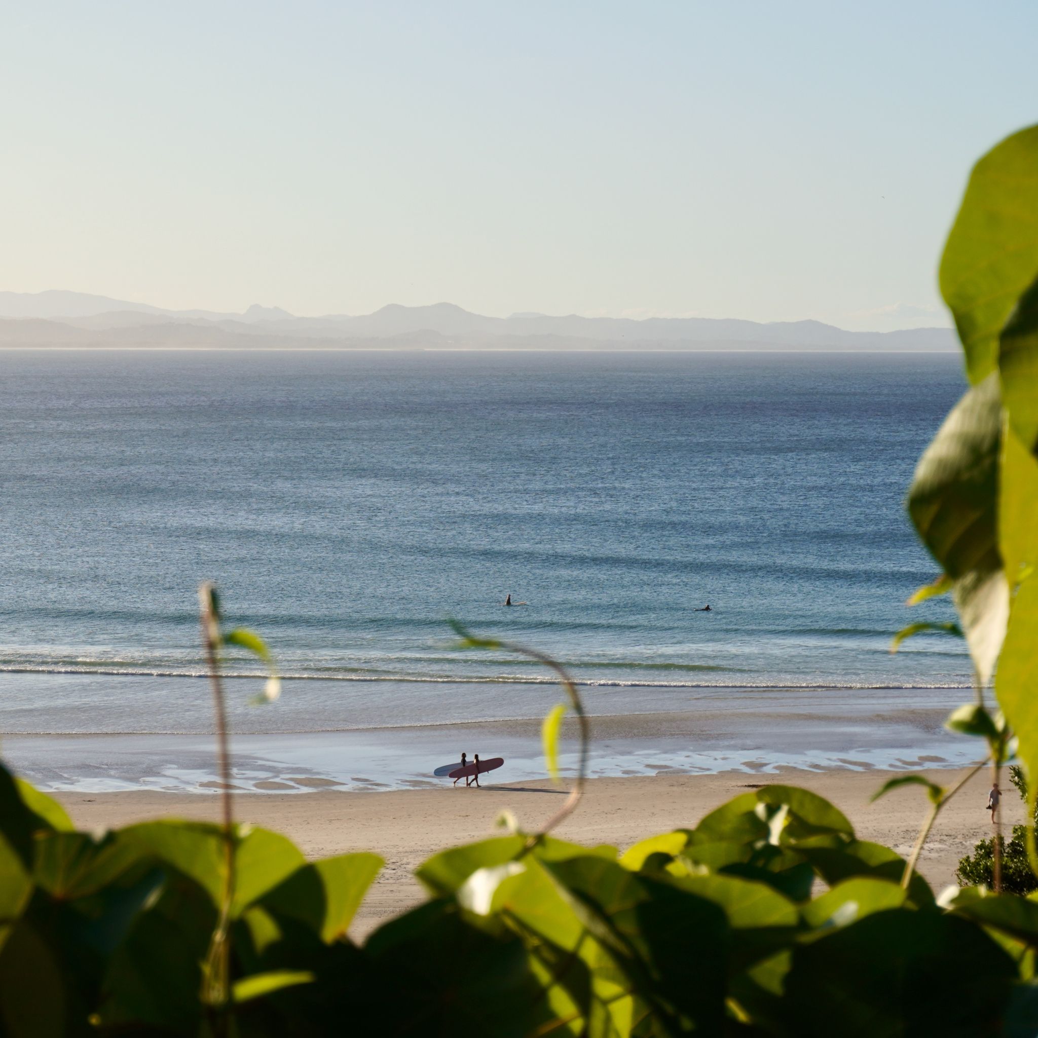 Two surfers walking on the beach with their board under their arm.