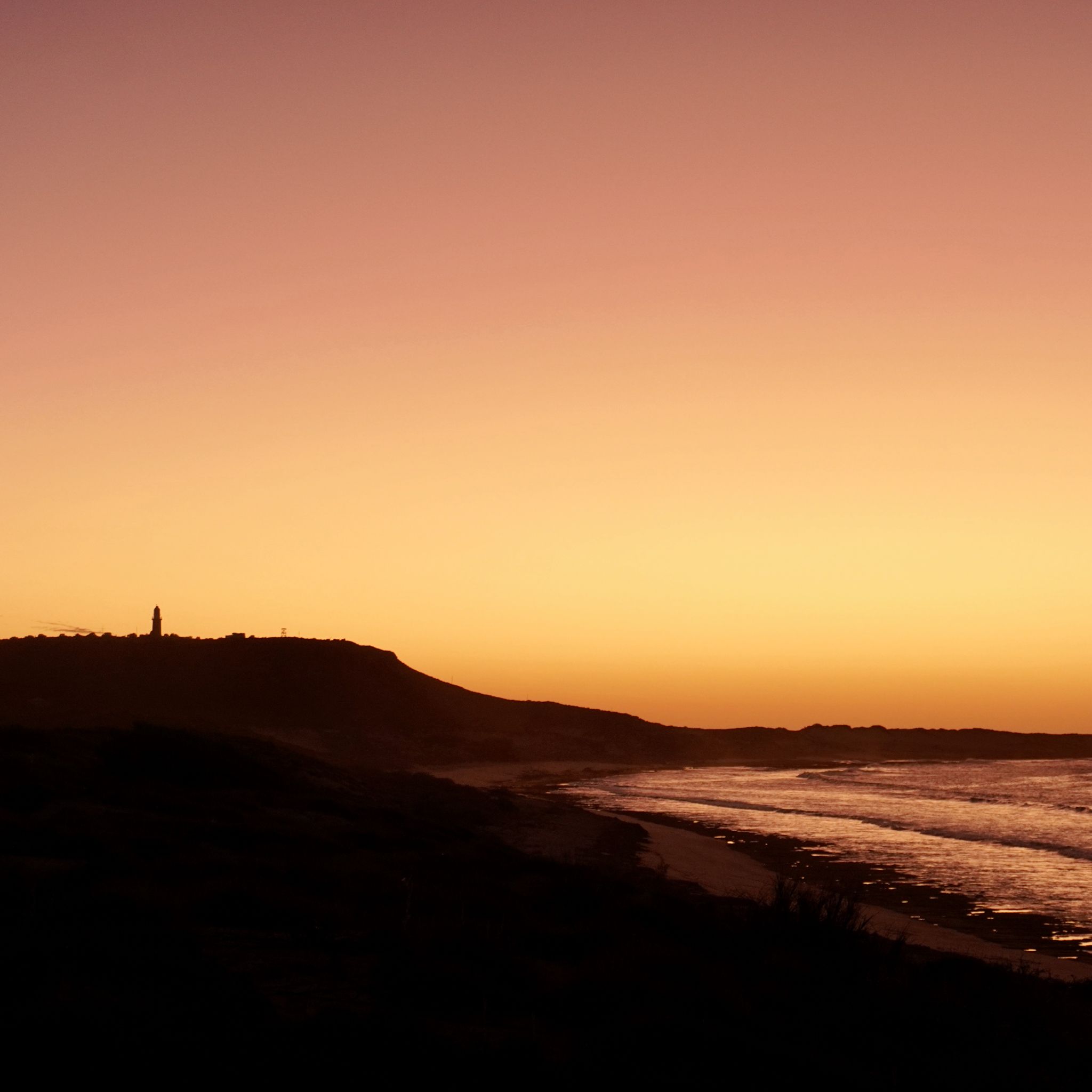 The sunset over the ocean photographed at Exmouth, with the silhouette of the lightouse in the background.