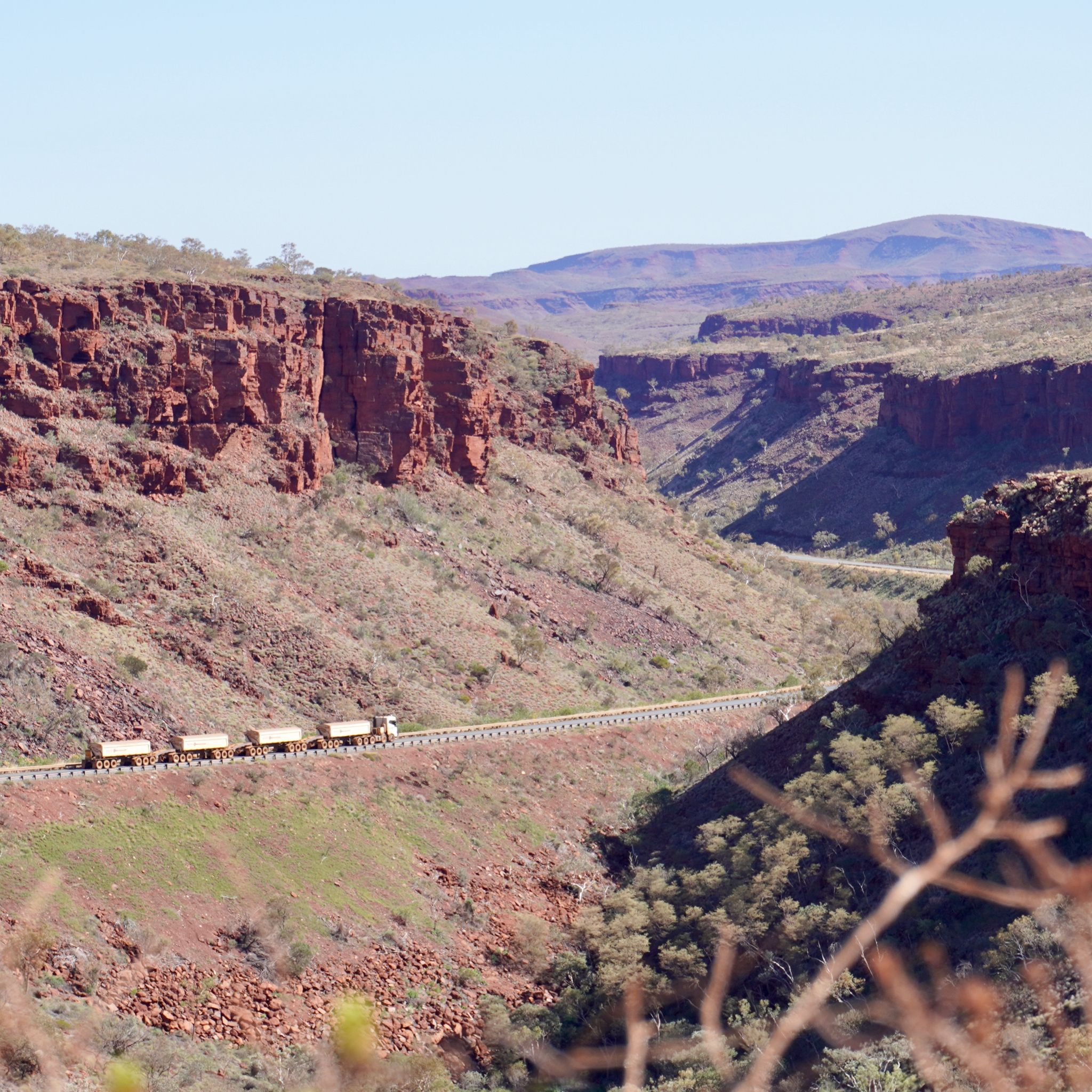 A road train carrying ore is driving through the red mountains in Western Australia.