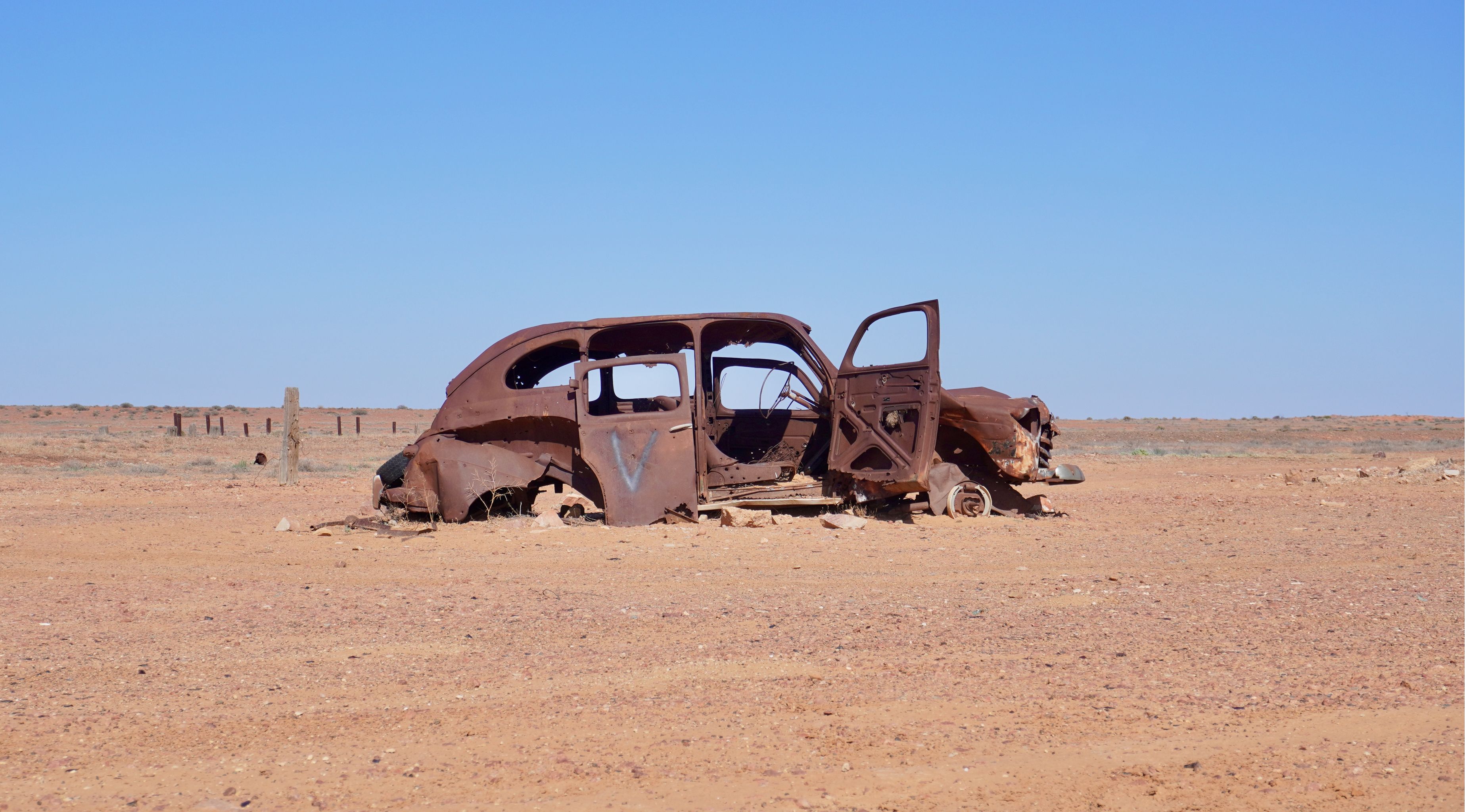 The rusty carcass of an abandonned car on the side of the road.