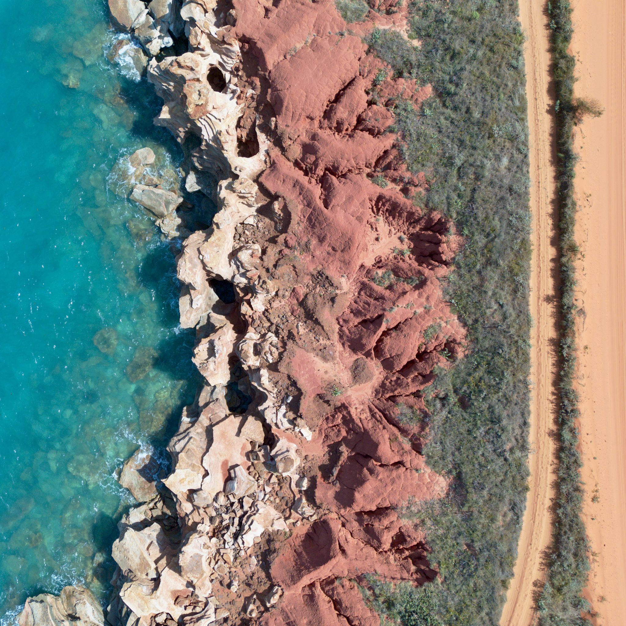 The orange cliffs meeting the turquoise sea photographed from above with a drone.