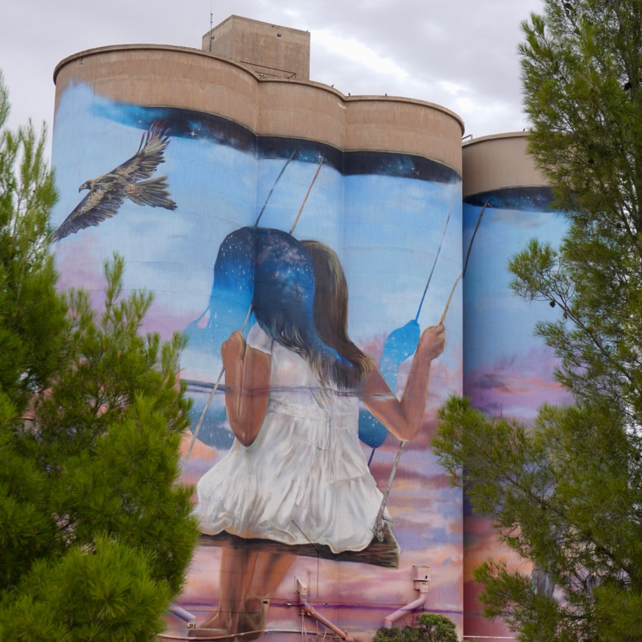 Four silos painted by Drapl & The Zookeeper representing a young girl on a swing.