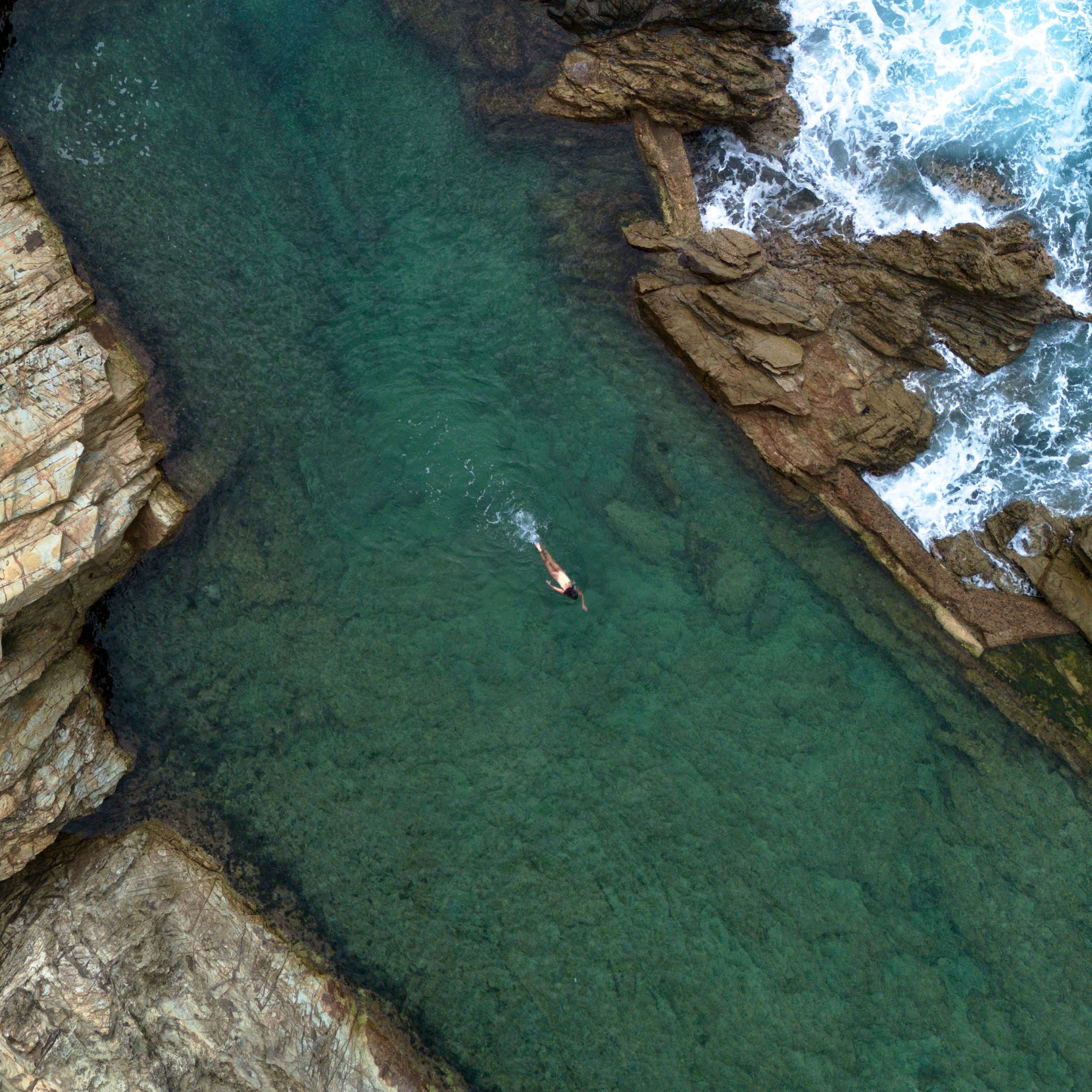 Bermagui's Blue Pool seen from above with a lone swimmer.