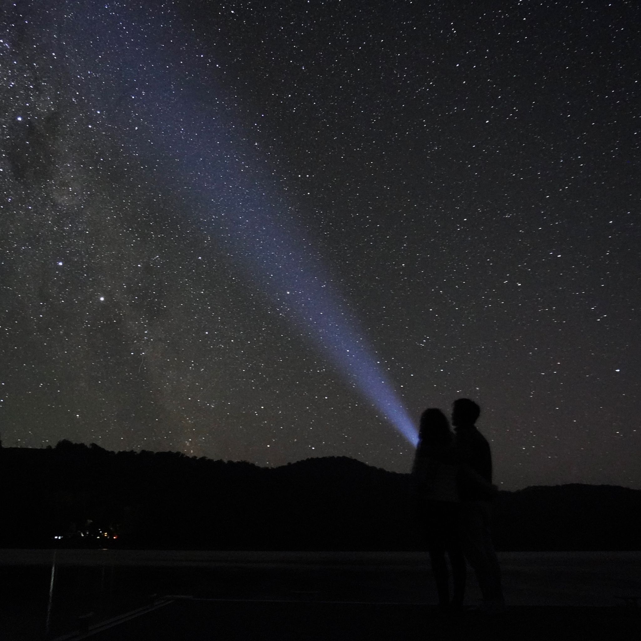 A starry night at Lake Barrington in Tasmania. We can see two people standing on a pontoon and flashing a light at the stars.