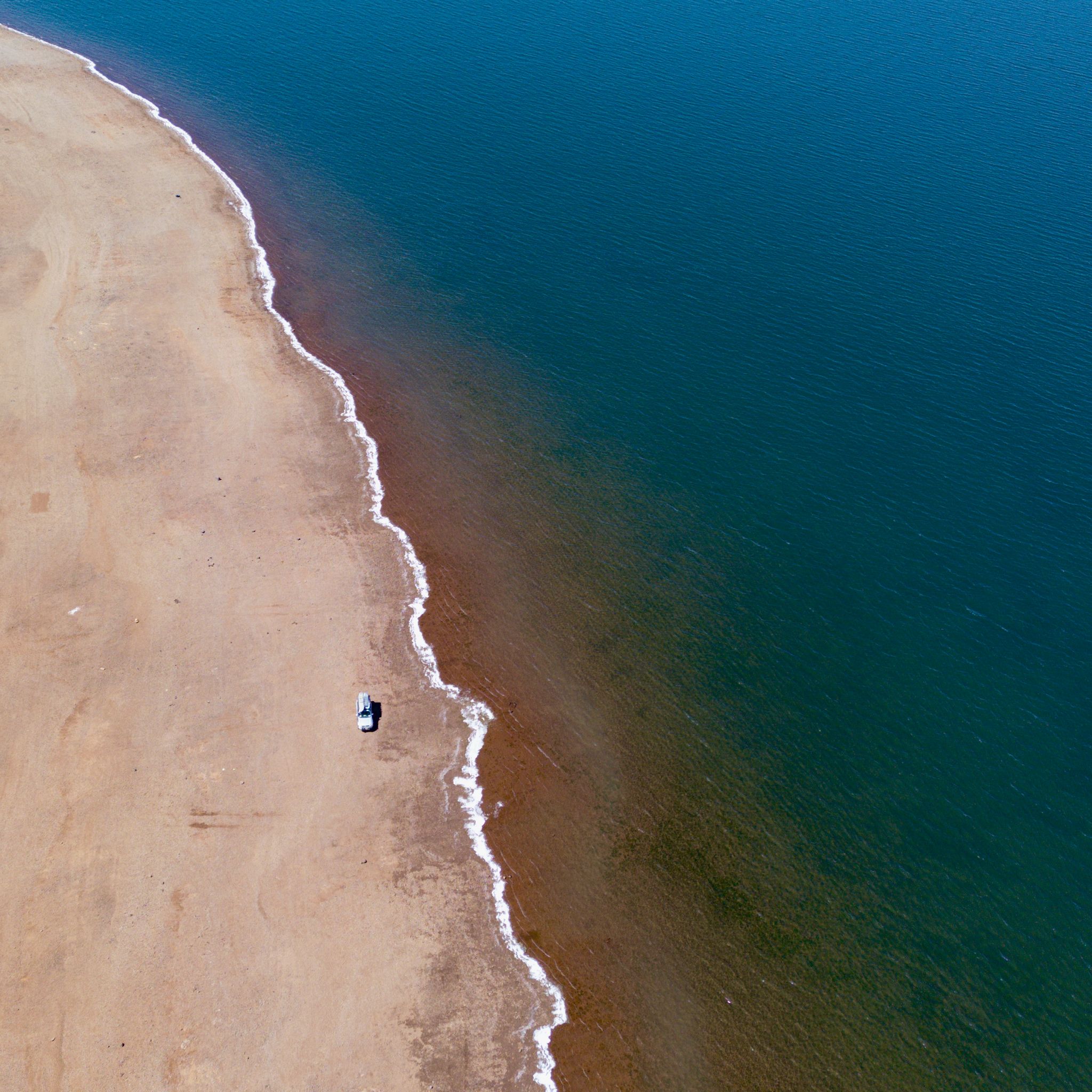 A picture taken from a drone of a car alongside the blue water of Yinga, the Great Lake.