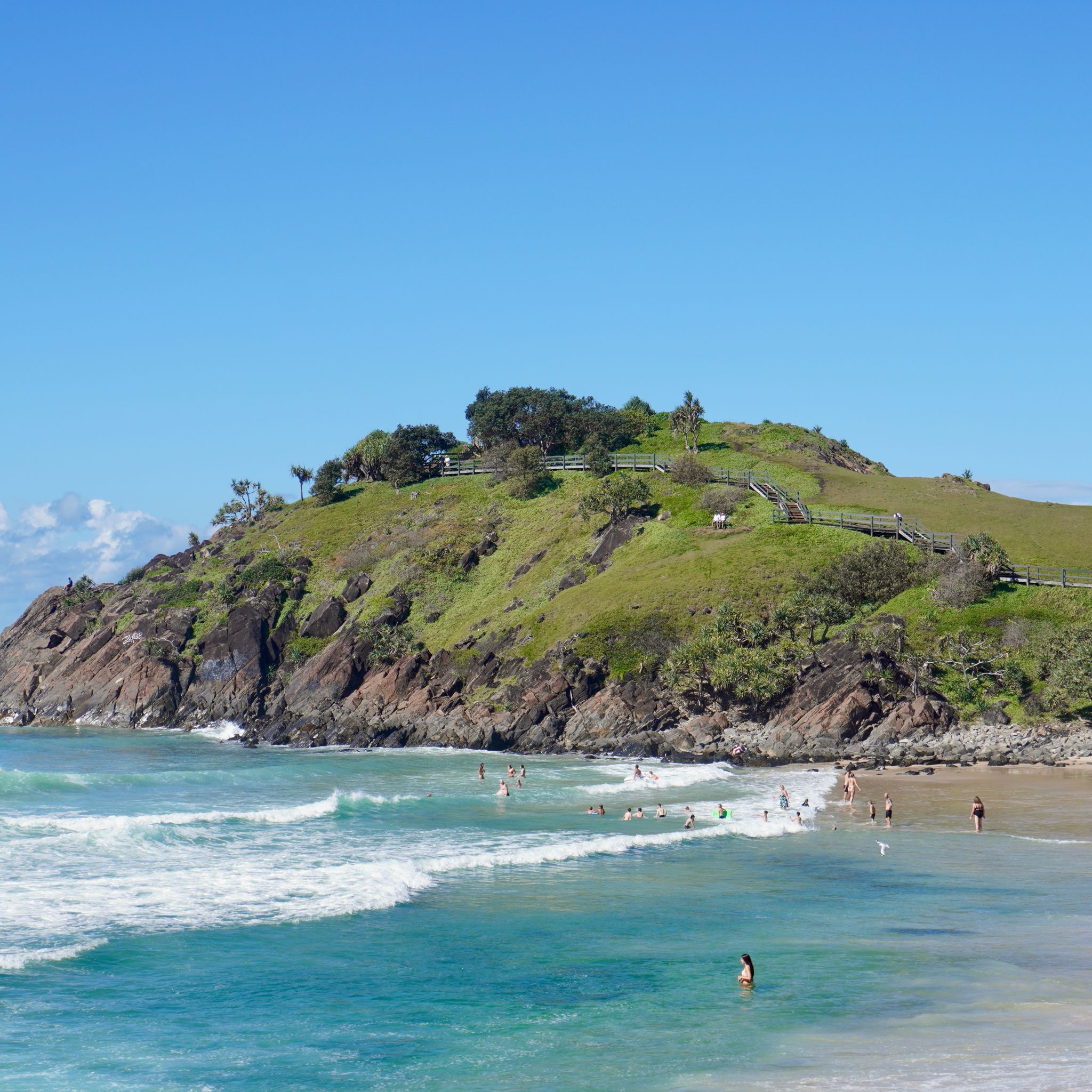 The rocky headland at Cabaret Beach in the background, with swimmers and beachgoers in the foreground.