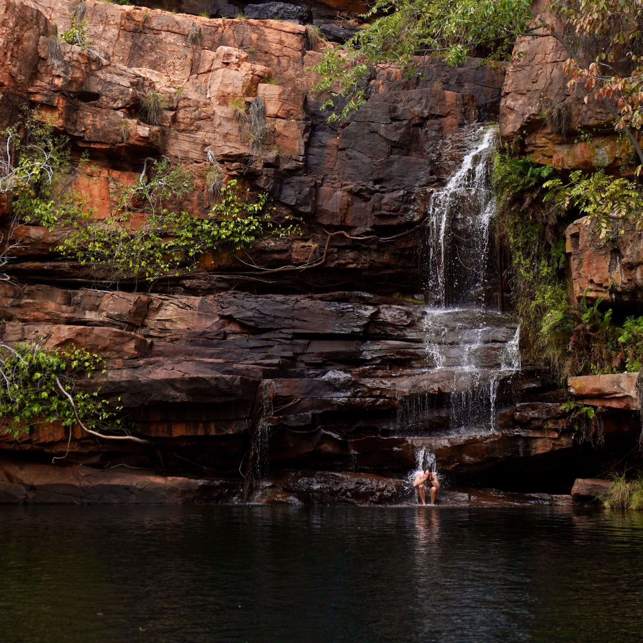 A waterfall where a man sits below the stream of water.